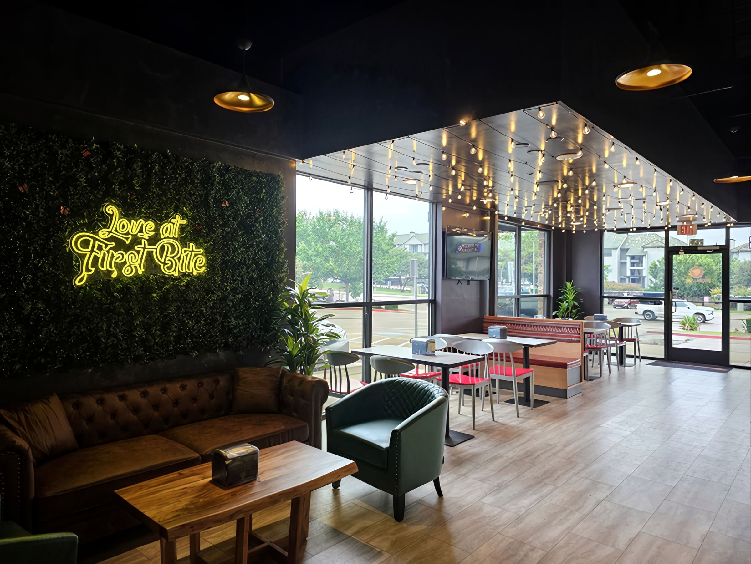 Pizza Twist dining room in Irving, Texas with wood slat ceiling, hanging greenery, and a neon Good Food Brings People Together sign